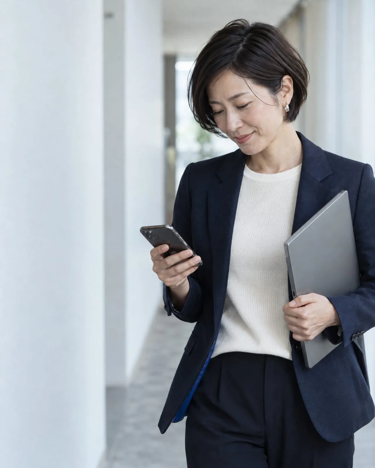 打ち合わせを終え、白い廊下でスマートフォンの記録を確かめる営業マネージャー（イメージ・見本）