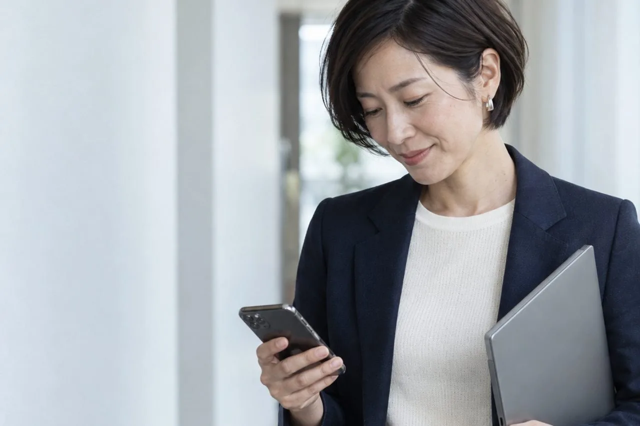 打ち合わせを終え、白い廊下でスマートフォンの記録を確かめる営業マネージャー（イメージ・見本）