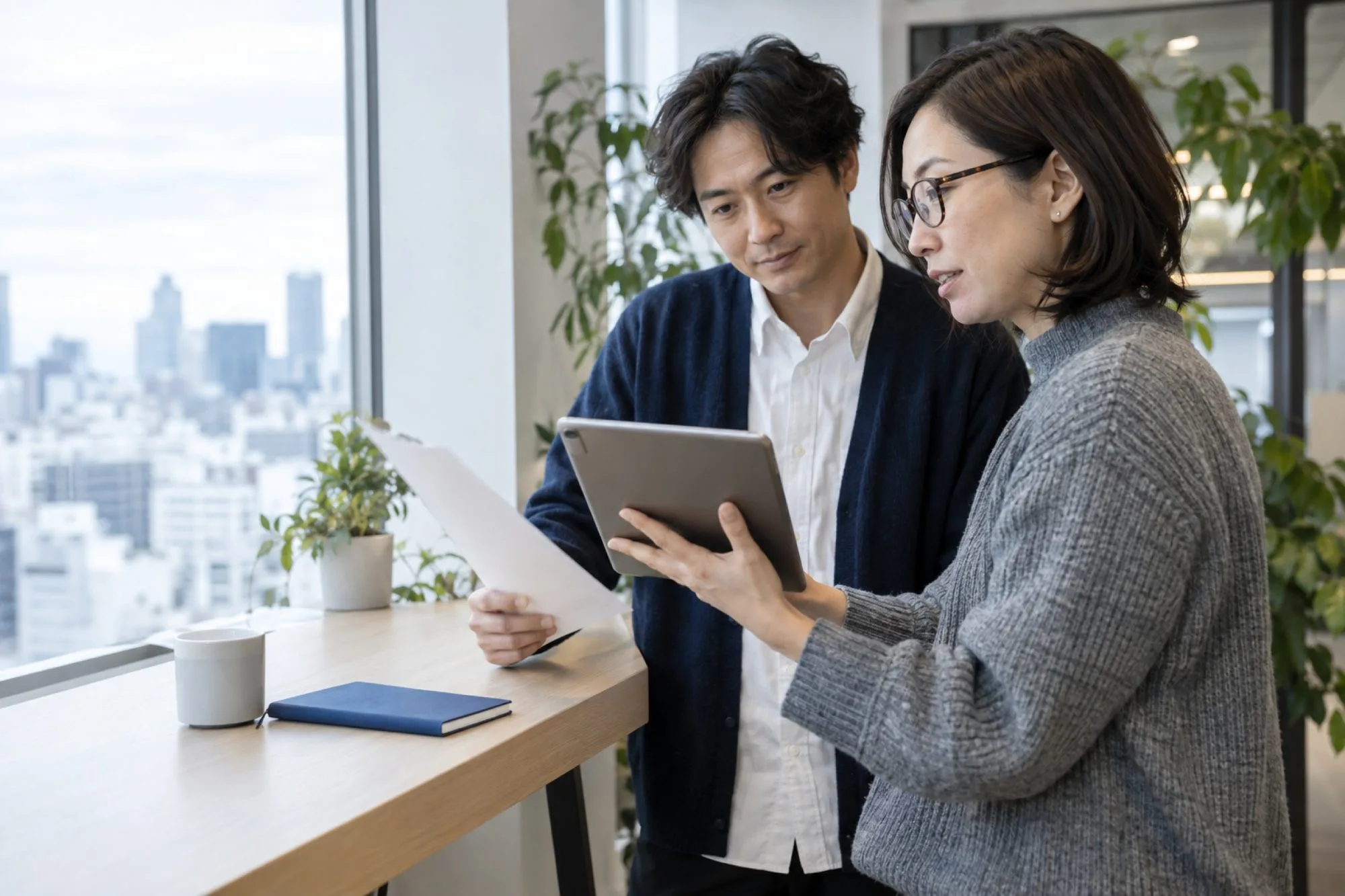 窓ぎわの机で、担当する会社の引き継ぎを確かめる 2 人の社員（イメージ・見本）